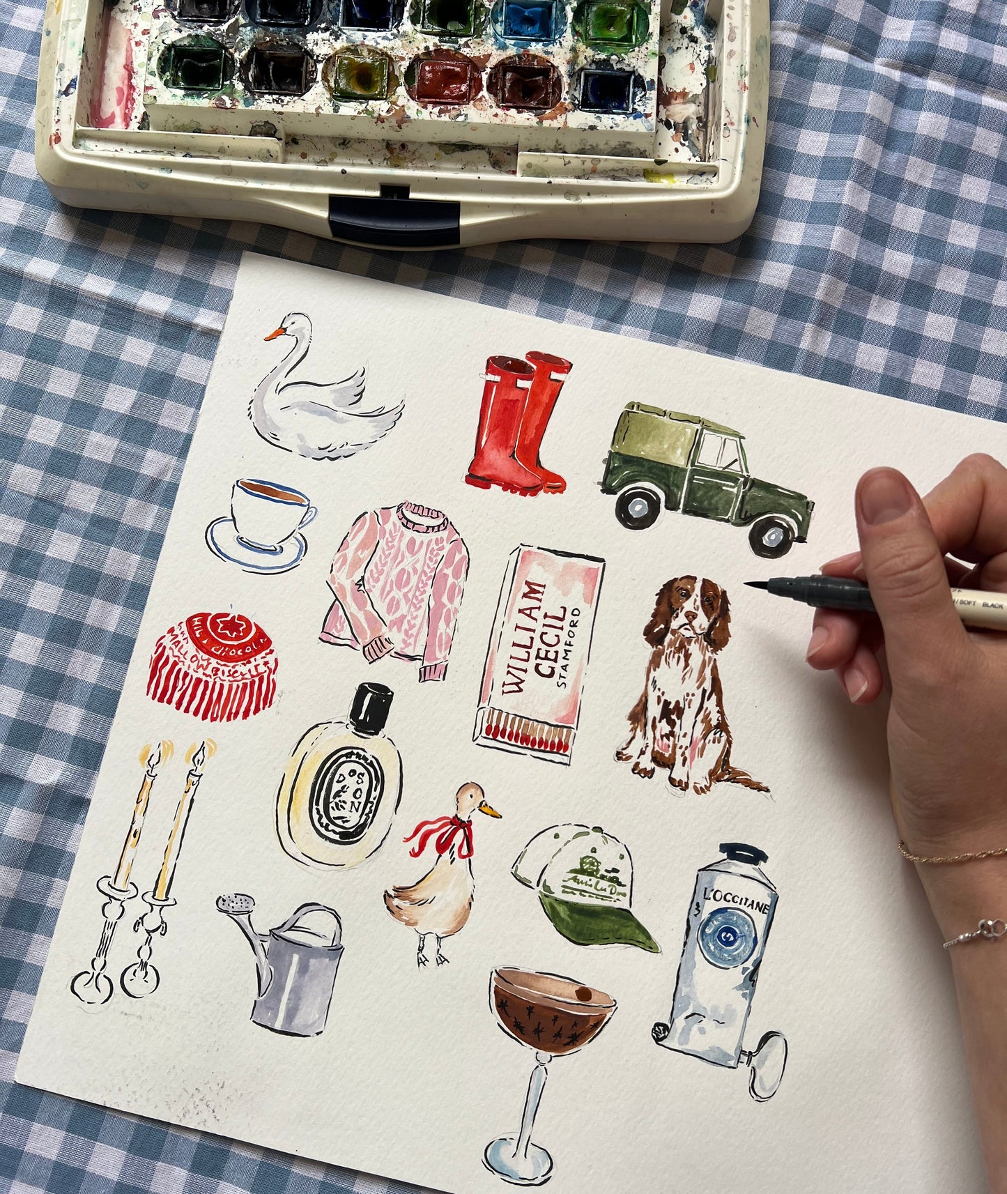 Artistic illustration of various objects on a checkered fabric background with watercolor set.